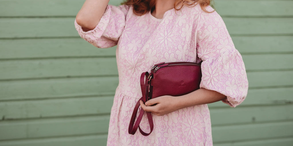 Lady in a pink dress holding small leather bag in her arms.