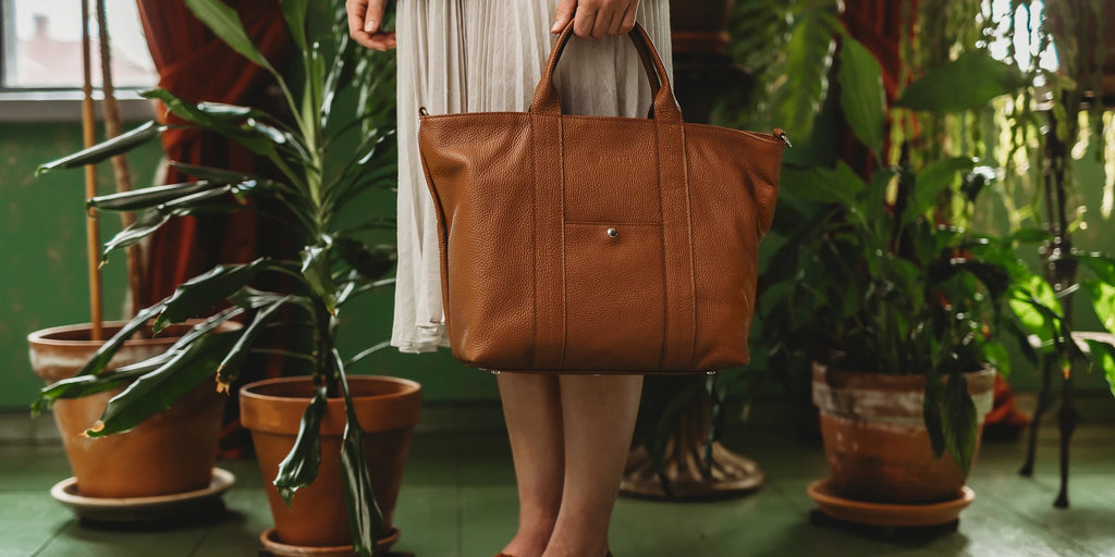 Lady and brown leather bag in front of green flowers