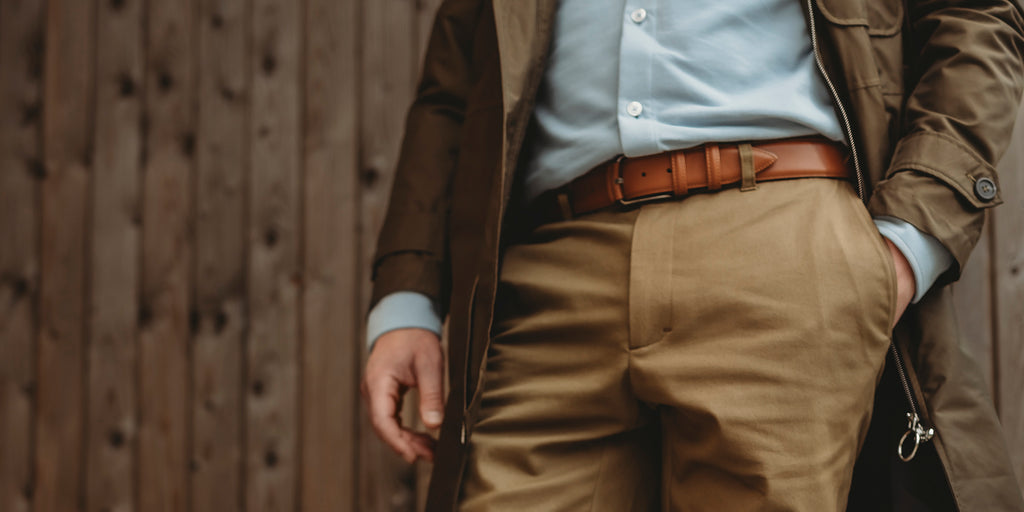 A man leaning to wall wearing genuine leather belt.
